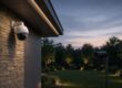 Dome camera under a building eave and a bullet camera overlooking a lit yard at dusk