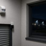 Motion detector high on a warehouse wall beside a roller door at night
